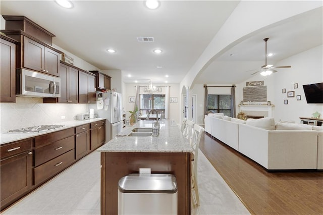 kitchen with light stone countertops, stainless steel appliances, ceiling fan, sink, and a center island with sink