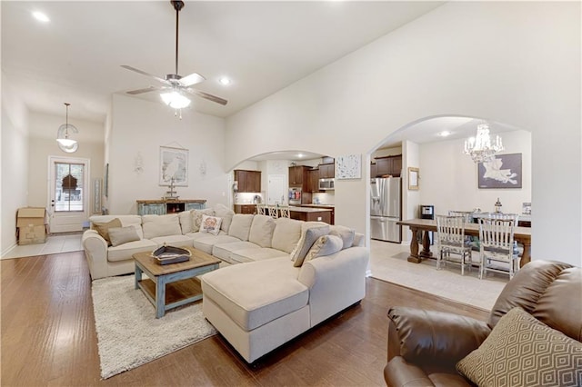 living room with ceiling fan with notable chandelier, wood-type flooring, and high vaulted ceiling