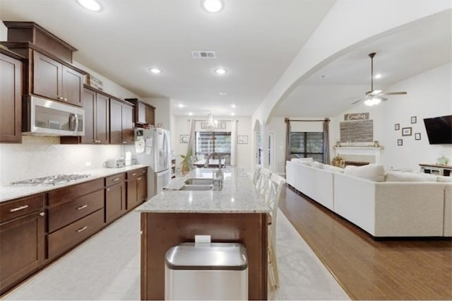 kitchen featuring appliances with stainless steel finishes, light wood-type flooring, ceiling fan, a kitchen island with sink, and sink