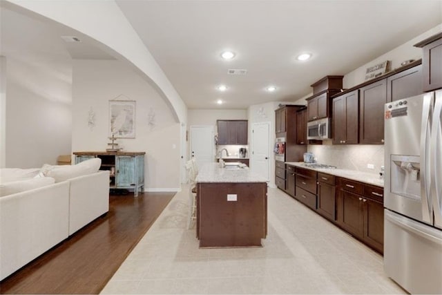 kitchen with appliances with stainless steel finishes, light wood-type flooring, dark brown cabinets, a kitchen island with sink, and sink