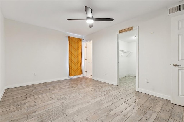 unfurnished bedroom with a walk in closet, light hardwood / wood-style flooring, ceiling fan, and a closet