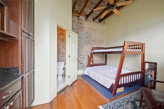 bedroom with ensuite bathroom, light hardwood / wood-style floors, beamed ceiling, and brick wall