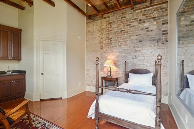 bedroom with wood-type flooring, beamed ceiling, brick wall, and a high ceiling