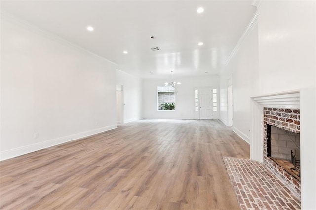 unfurnished living room featuring crown molding, light hardwood / wood-style flooring, a chandelier, and a brick fireplace