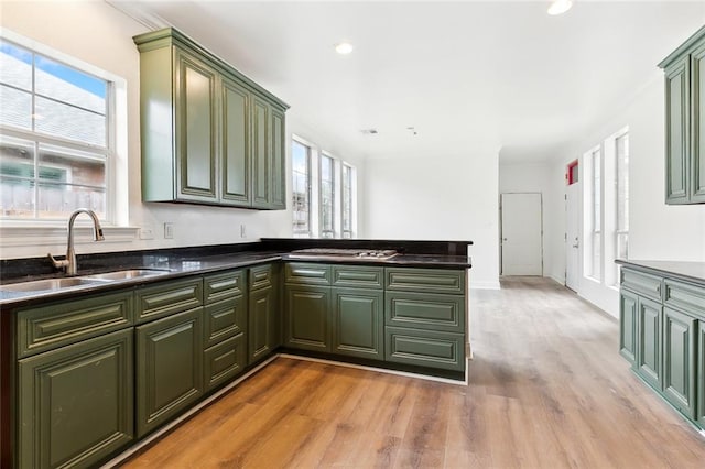 kitchen with green cabinets, kitchen peninsula, sink, and light hardwood / wood-style flooring