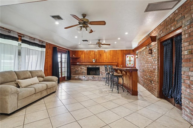 3733 Rockford Hts, Metairie, LA 70002 - living room featuring brick wall, ceiling fan, wooden walls, light tile patterned floors, and a fireplace