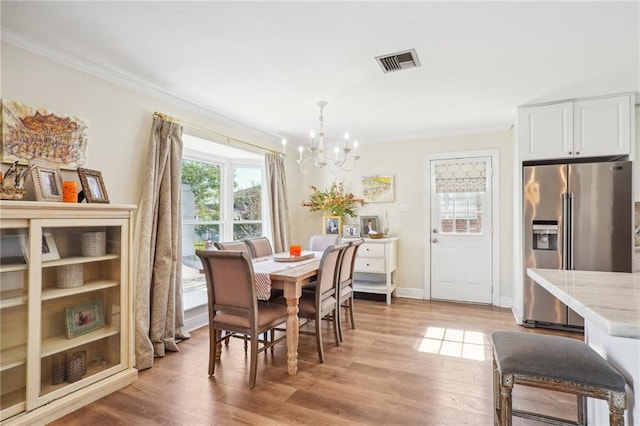 dining room with light wood-type flooring, crown molding, and a notable chandelier