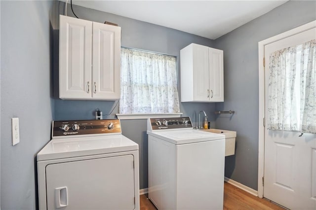 clothes washing area with washer and clothes dryer, a healthy amount of sunlight, cabinets, and light hardwood / wood-style flooring