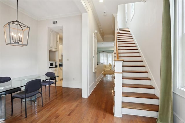 stairway with a notable chandelier, wood-type flooring, and crown molding