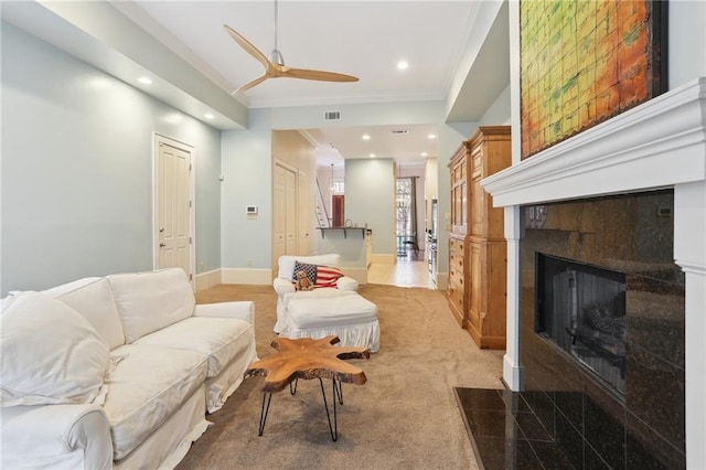 carpeted living room with ceiling fan, crown molding, and a fireplace