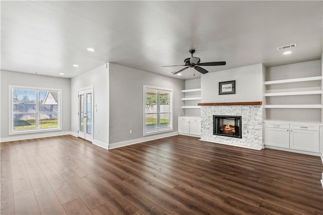 unfurnished living room featuring ceiling fan, dark hardwood / wood-style floors, built in features, and a stone fireplace