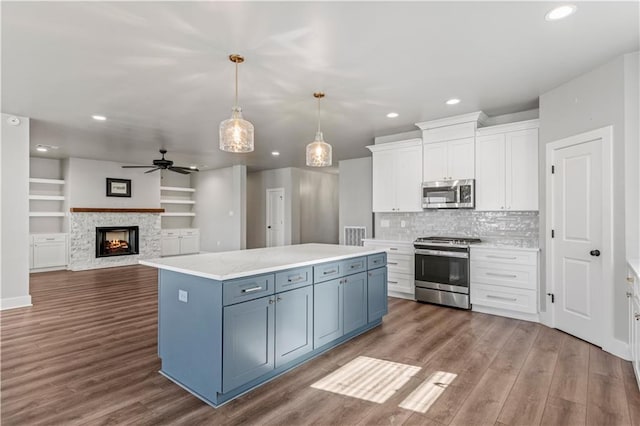 kitchen with pendant lighting, white cabinets, built in shelves, a kitchen island, and stainless steel appliances