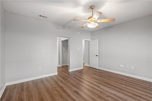 unfurnished bedroom featuring a textured ceiling, a walk in closet, wood-type flooring, a closet, and ceiling fan