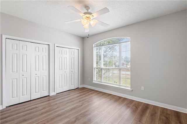 unfurnished bedroom featuring light hardwood / wood-style floors, a textured ceiling, two closets, and ceiling fan