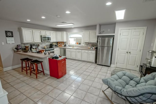 kitchen with a kitchen breakfast bar, kitchen peninsula, white cabinets, and appliances with stainless steel finishes