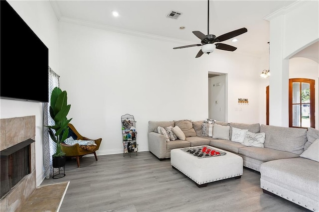 living room featuring ceiling fan, a tiled fireplace, ornamental molding, and hardwood / wood-style floors