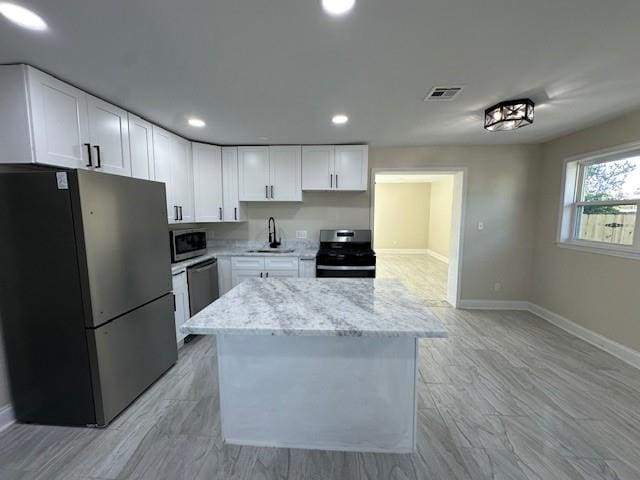 kitchen with appliances with stainless steel finishes, light stone counters, sink, white cabinets, and a kitchen island