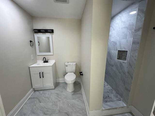 bathroom with a tile shower, vanity, and toilet