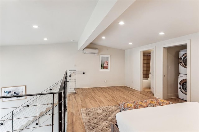 bedroom featuring a wall mounted air conditioner, a spacious closet, light hardwood / wood-style floors, stacked washer / dryer, and a closet