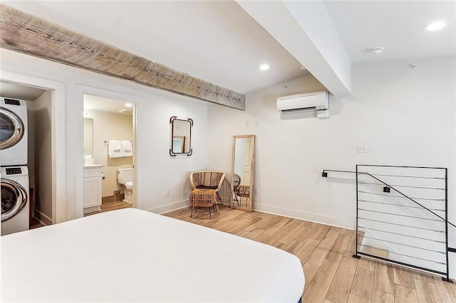 bedroom with light hardwood / wood-style floors, stacked washer and dryer, a wall unit AC, and connected bathroom