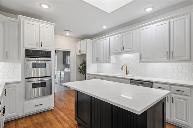 kitchen with stainless steel appliances, sink, washing machine and dryer, light hardwood / wood-style floors, and white cabinetry