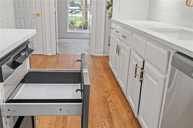 kitchen featuring white cabinetry, dishwasher, light wood-type flooring, and sink