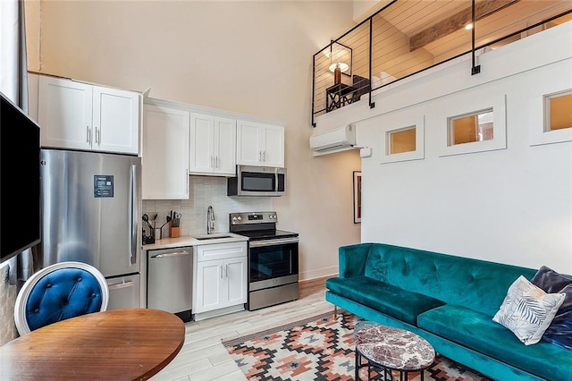 living area with a wall mounted air conditioner, a high ceiling, and light wood finished floors