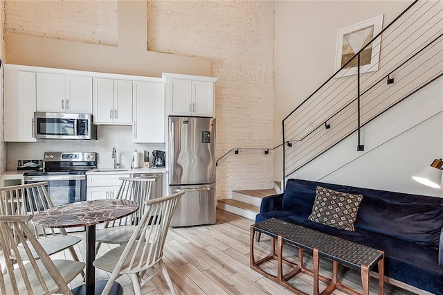 kitchen with a sink, stainless steel appliances, decorative backsplash, light wood-style flooring, and a towering ceiling