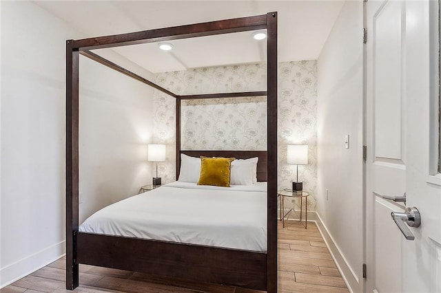 bedroom with recessed lighting, wallpapered walls, wood finished floors, and baseboards
