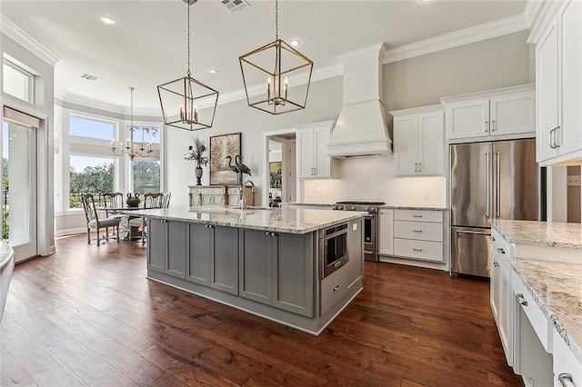 kitchen featuring pendant lighting, premium appliances, custom range hood, and white cabinets