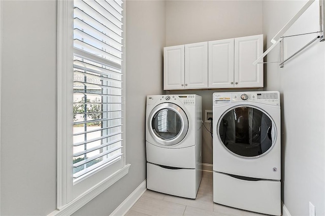 clothes washing area featuring cabinets, light tile patterned flooring, and washing machine and clothes dryer