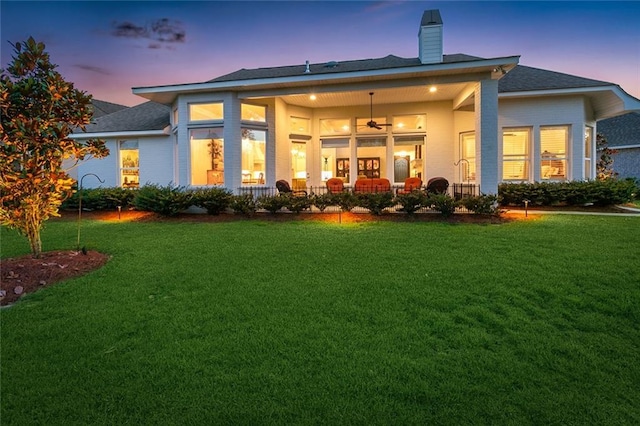 back house at dusk with ceiling fan and a lawn