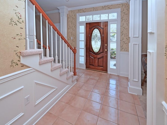 foyer entrance with decorative columns, crown molding, light tile patterned floors, a wainscoted wall, and wallpapered walls