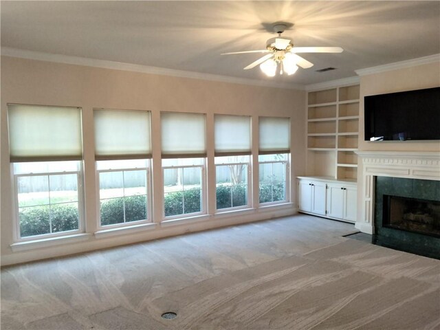 unfurnished living room featuring ceiling fan, a fireplace, ornamental molding, light carpet, and built in shelves