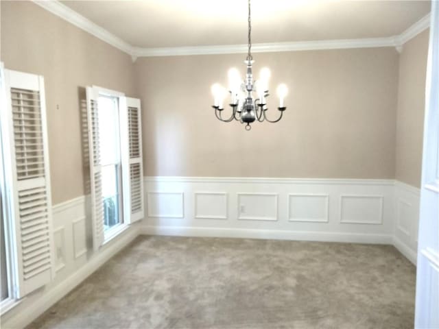 empty room featuring an inviting chandelier, carpet, crown molding, and a wainscoted wall