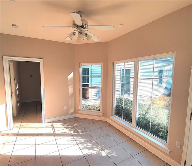 empty room with baseboards, a ceiling fan, light tile patterned floors, and a wealth of natural light