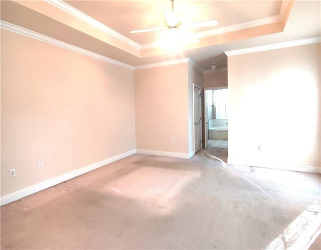 empty room featuring a raised ceiling, ornamental molding, baseboards, and light colored carpet