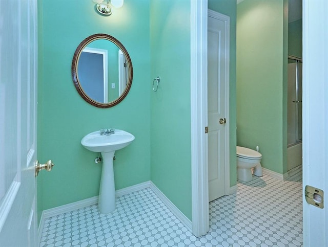 bathroom featuring toilet, baseboards, and a shower with shower door