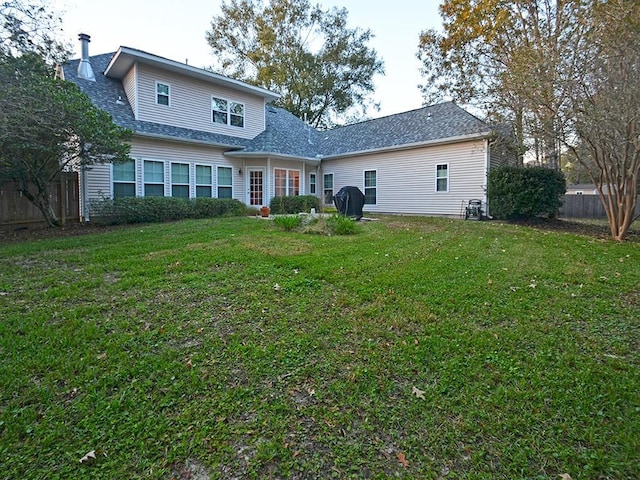 rear view of house with roof with shingles, fence, and a yard
