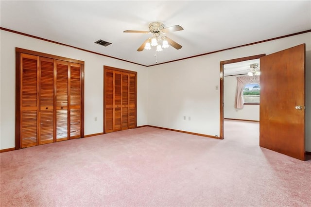 unfurnished bedroom featuring ceiling fan, light colored carpet, ornamental molding, and two closets