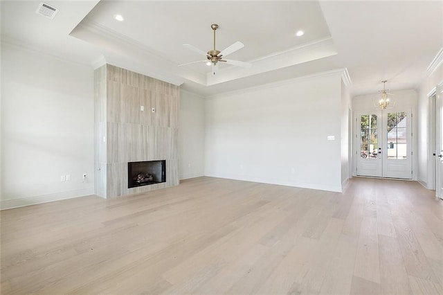 unfurnished living room featuring a large fireplace, a raised ceiling, and light wood-type flooring