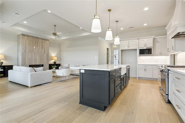 kitchen featuring pendant lighting, white cabinetry, a tray ceiling, an island with sink, and stainless steel range oven