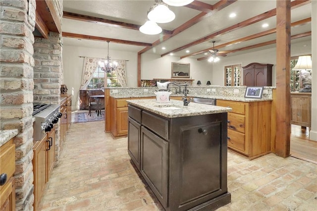 kitchen with beam ceiling, sink, light stone counters, an island with sink, and pendant lighting