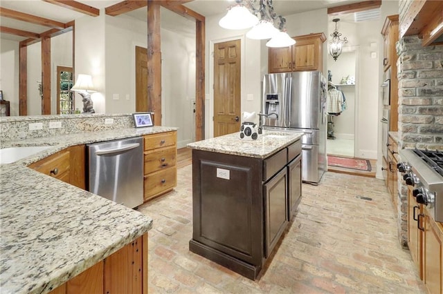 kitchen with beam ceiling, light stone counters, decorative light fixtures, a center island with sink, and appliances with stainless steel finishes