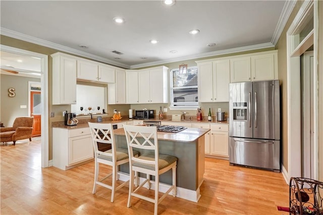 kitchen with a breakfast bar, stainless steel appliances, light hardwood / wood-style flooring, white cabinets, and a center island