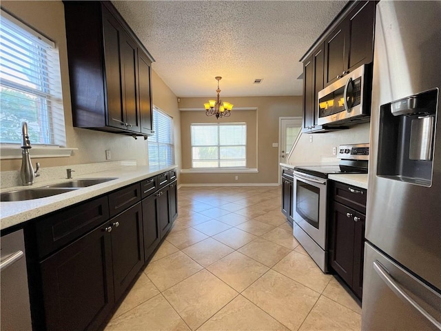 kitchen with a textured ceiling, stainless steel appliances, sink, pendant lighting, and a notable chandelier