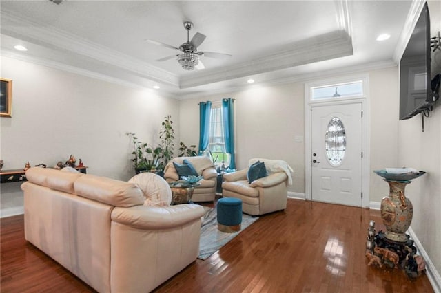 living room featuring hardwood / wood-style flooring, a raised ceiling, ceiling fan, and ornamental molding