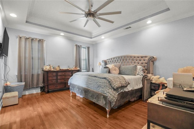 bedroom with wood-type flooring, a raised ceiling, ceiling fan, and crown molding