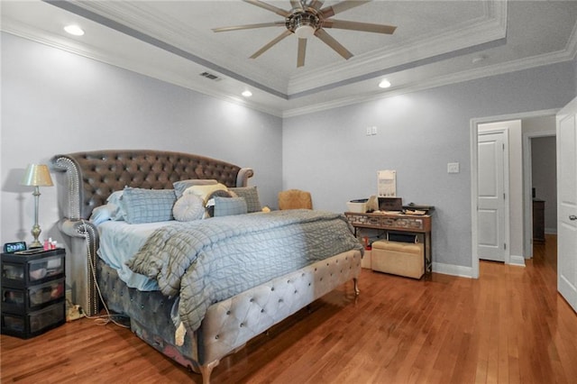 bedroom featuring hardwood / wood-style floors, ceiling fan, crown molding, and a tray ceiling