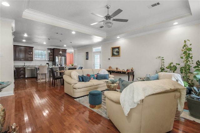 living room with ornamental molding, a raised ceiling, ceiling fan, and dark wood-type flooring